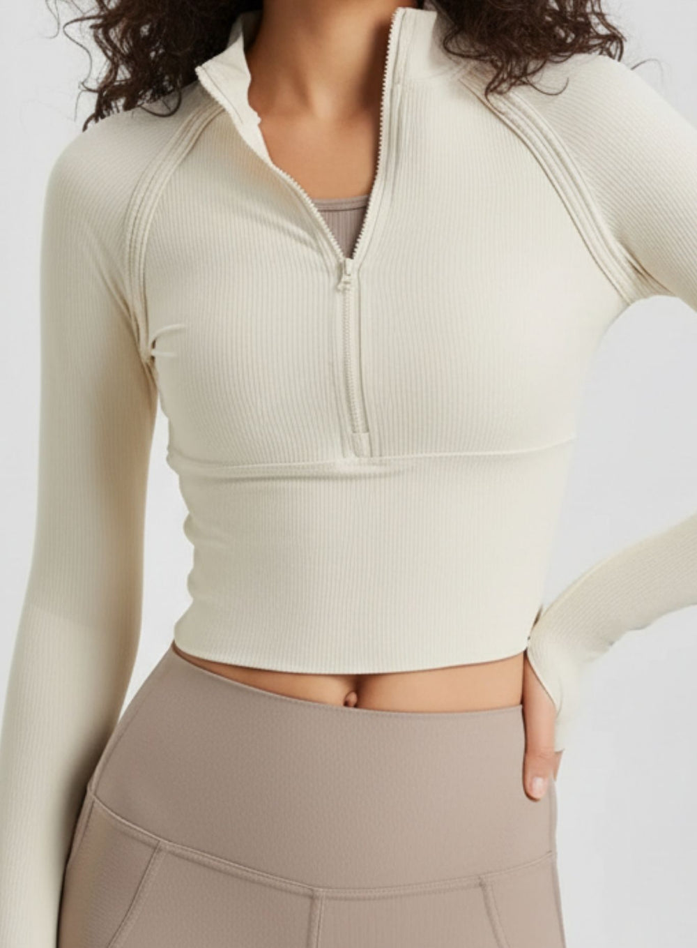 Model unzipping ivory half-zip long-sleeve crop top, 4-way stretch performance knit.